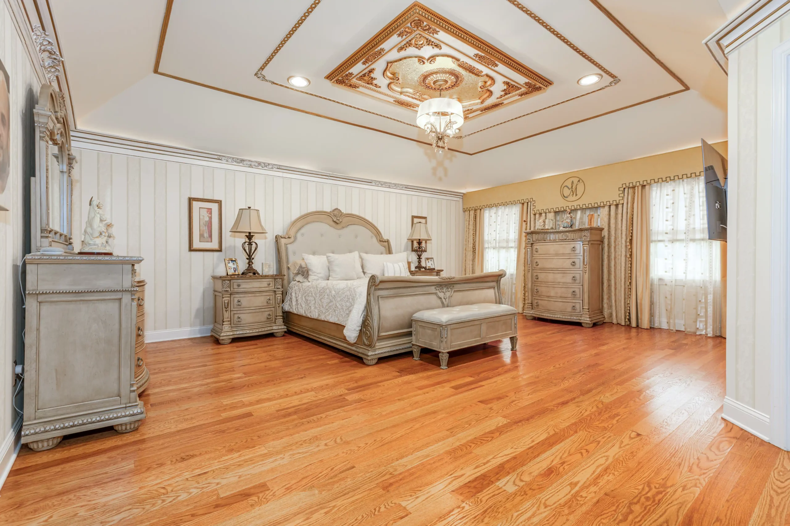 A beautifully designed bedroom with a large bed and a stunning chandelier, captured by a real estate photographer.